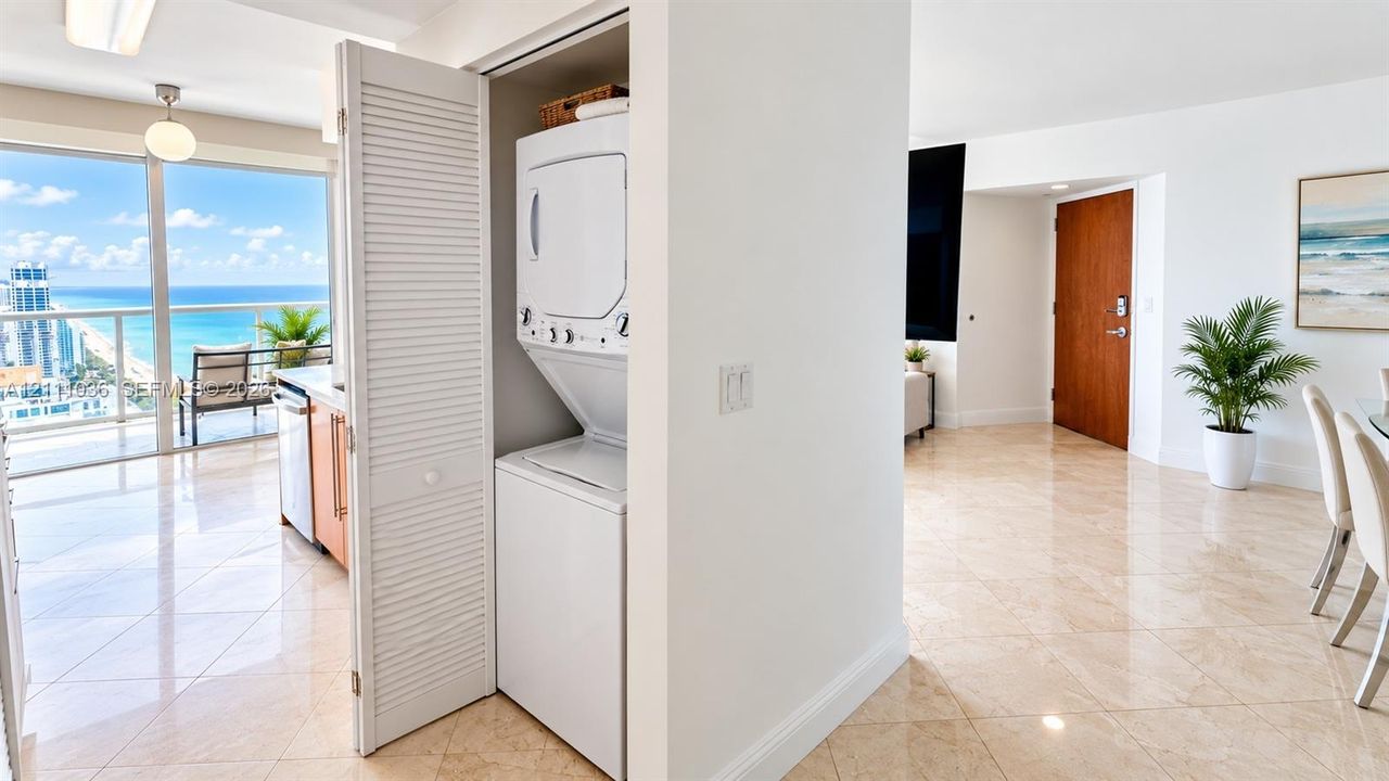 In-unit laundry closet featuring white louvered folding doors, floor-to-ceiling glass paneling, tile flooring, and a solid-core wood entry door