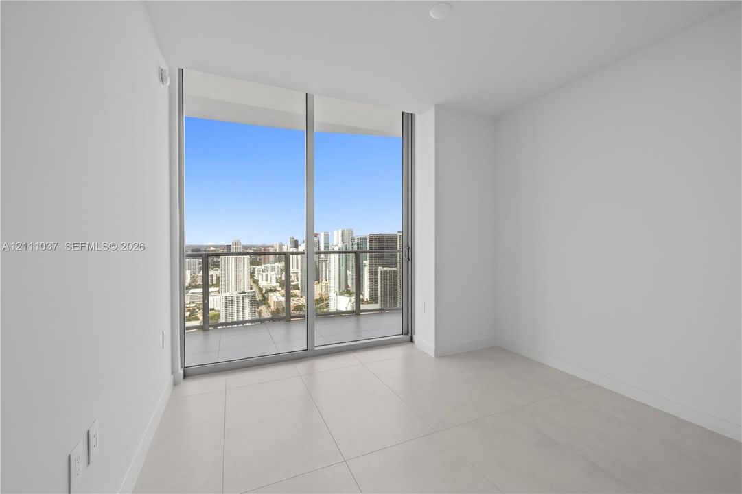Floor-to-ceiling sliding glass doors, private balcony with metal and glass railing, and large-format porcelain tile flooring
