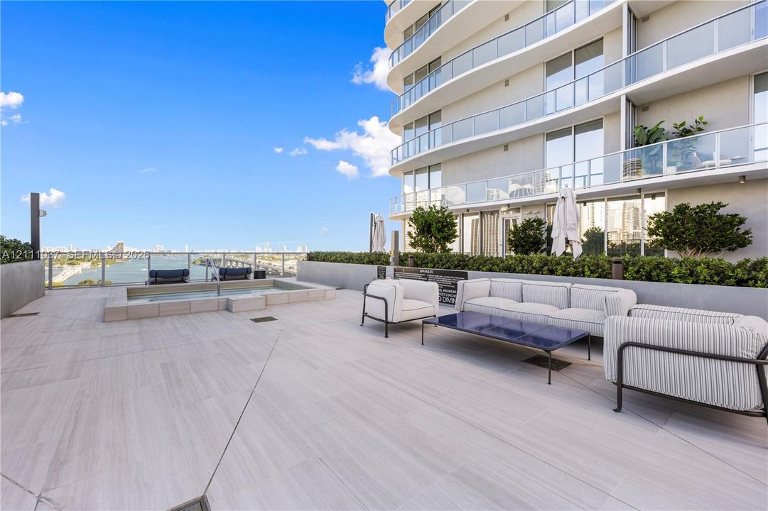 Expansive elevated terrace featuring large-format porcelain tile flooring, a rectangular built-in soaking pool, concrete perimeter walling, and glass balcony railings
