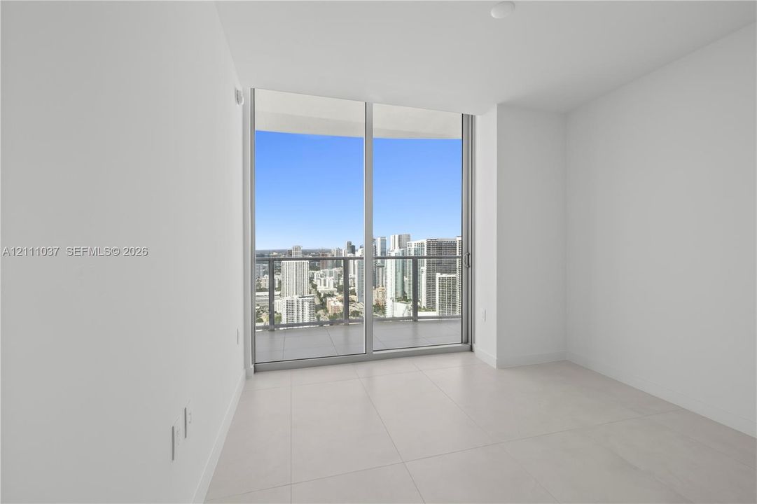 Floor-to-ceiling glass sliding doors, large-format tile flooring, and a private balcony featuring a glass panel railing