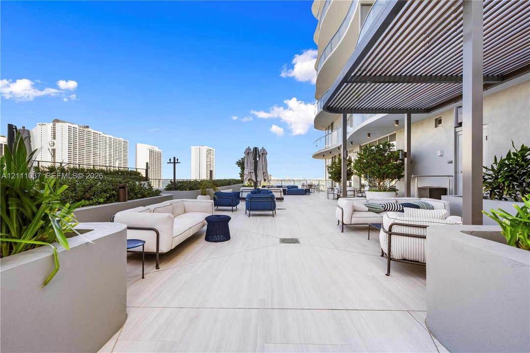 Expansive outdoor terrace featuring large-format tile flooring, a structured metal pergola, built-in concrete planters, and glass balcony railings