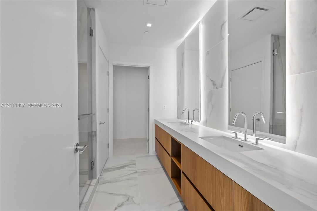 Floating wood-finish vanity with a stone-surfaced countertop, integrated double sinks, polished chrome fixtures, full-height tile backsplash, and LED-backlit mirrors