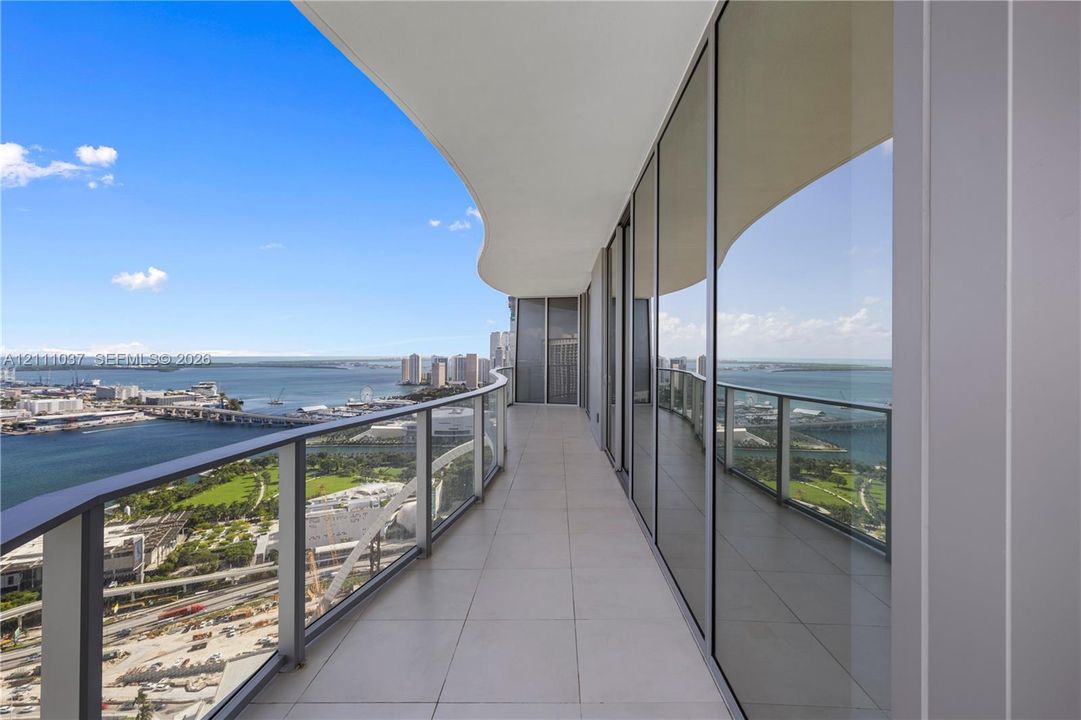 Curved balcony featuring large-format tile flooring, a glass panel railing, and full-height floor-to-ceiling glass wall enclosures