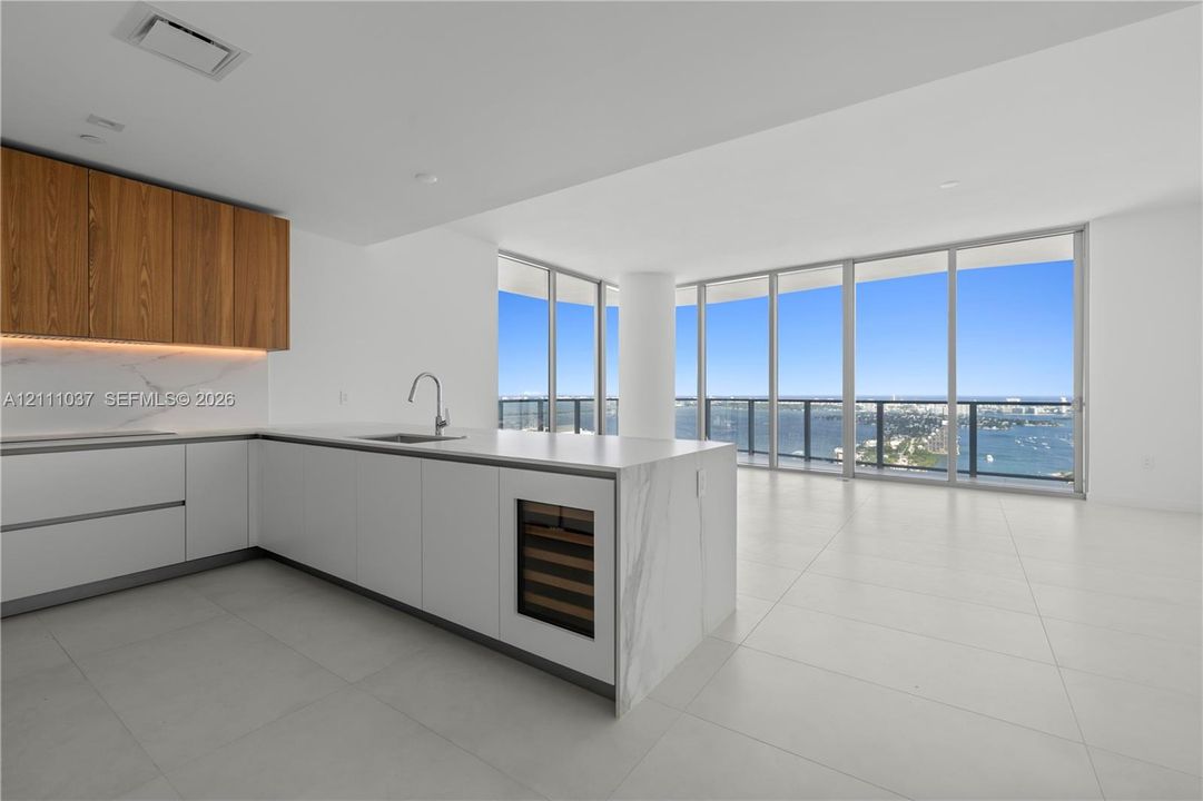 Kitchen featuring flat-panel cabinetry, a stone-surfaced island with an integrated wine refrigerator, large-format tile flooring, and floor-to-ceiling windows