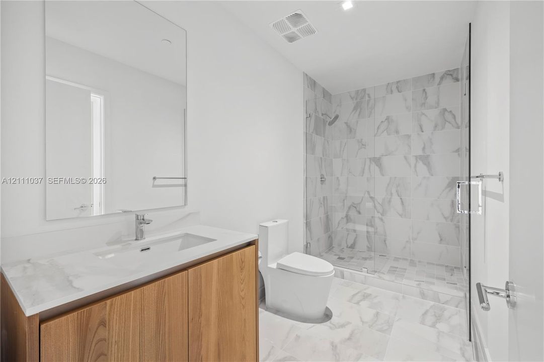 Wood-finish vanity with a rectangular sink, expansive mirror, walk-in shower with floor-to-ceiling tile, and tiled flooring