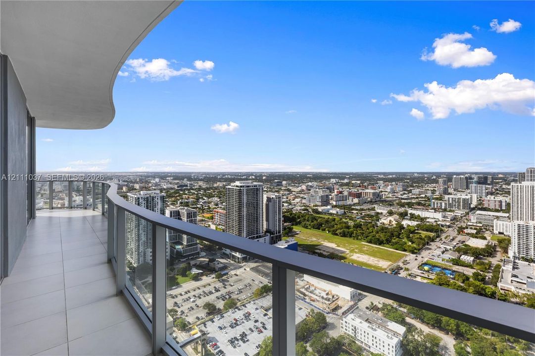 Covered balcony featuring oversized tile flooring, a curved architectural ceiling, and a full-length glass railing