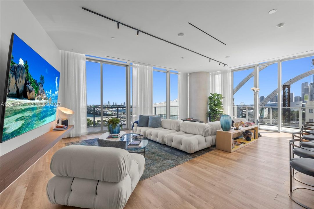 Floor-to-ceiling glass walls, wood-finish flooring, floating wood-finish media console, recessed linear lighting, and architectural concrete column