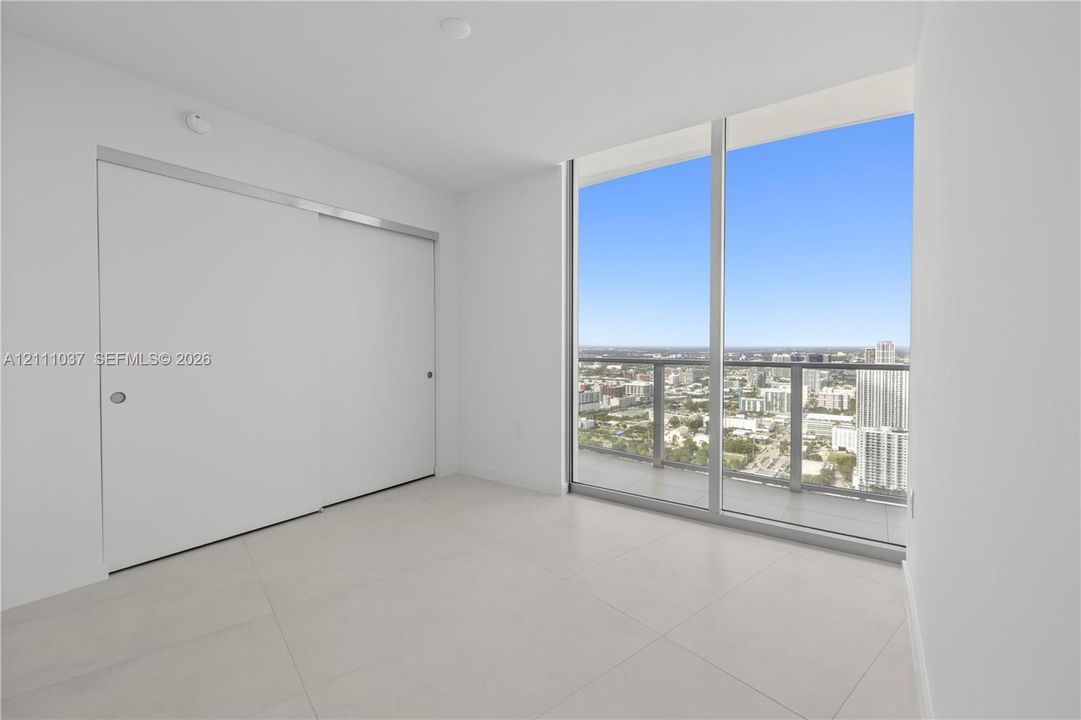 Floor-to-ceiling glass windows, sliding closet doors, and large-format tile flooring
