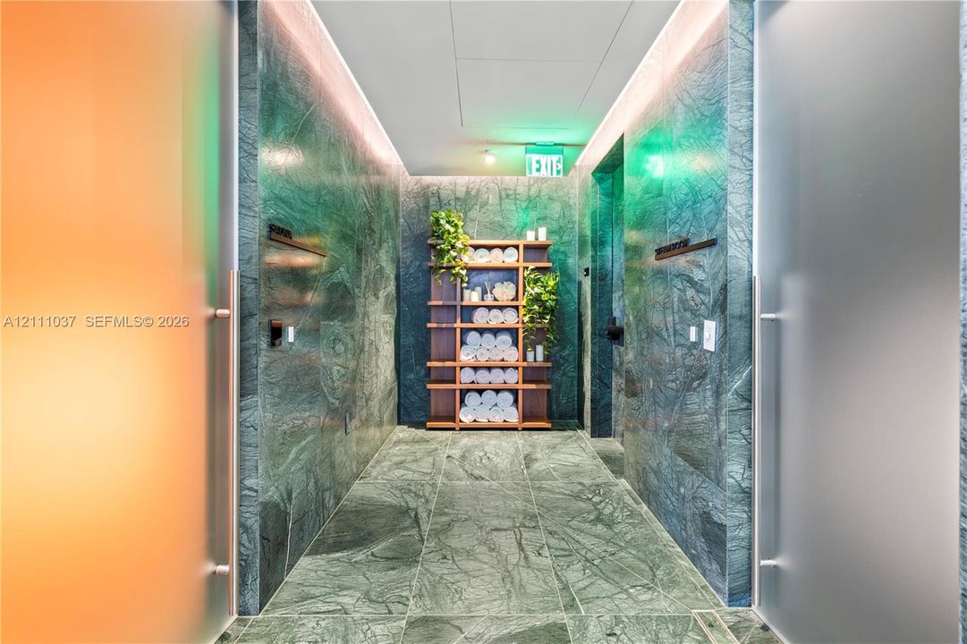 Hallway featuring floor-to-ceiling green stone wall cladding, matching stone tile flooring, recessed cove lighting, and built-in open wood shelving