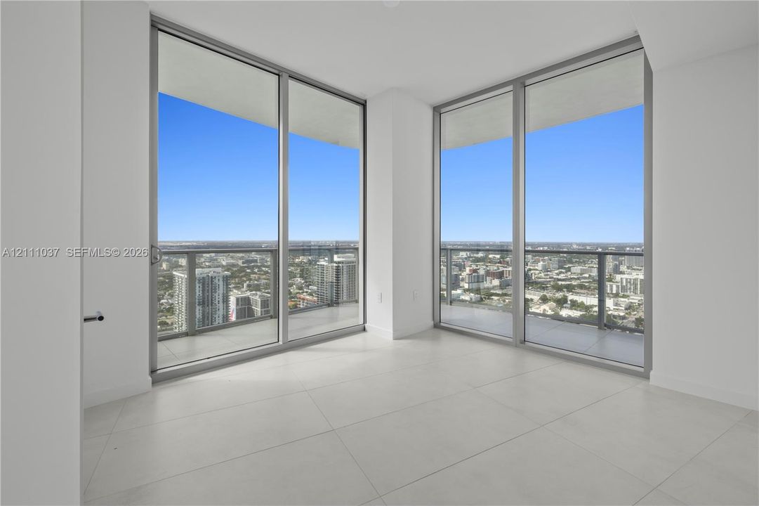 Floor-to-ceiling glass windows, wraparound balconies with metal and glass railings, and neutral tile flooring