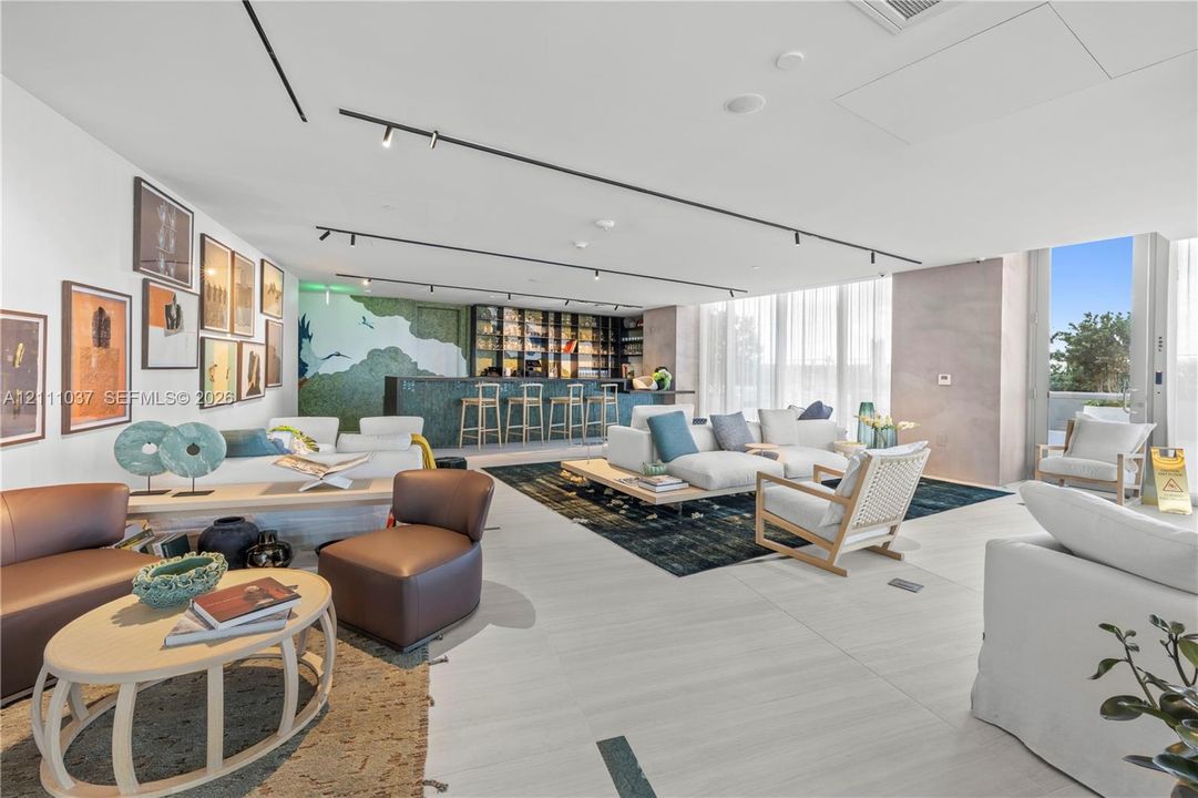 Open-concept interior featuring light-toned tile flooring, recessed track lighting, and a built-in wet bar with glass shelving and a decorative backsplash