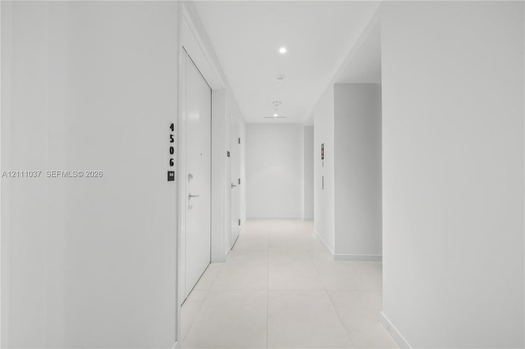 Interior hallway featuring large-format tile flooring, recessed ceiling lighting, and crisp white wall finishes