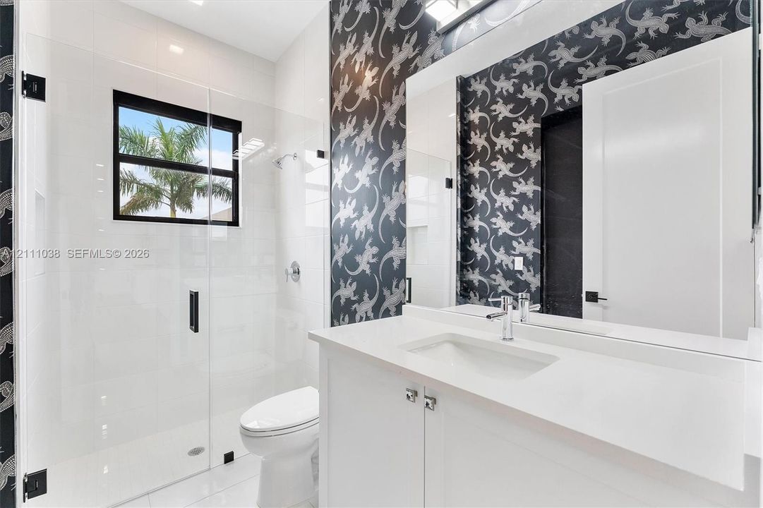 Bathroom featuring a white vanity with a quartz countertop, frameless glass-enclosed shower, polished chrome fixtures, and patterned wallcovering