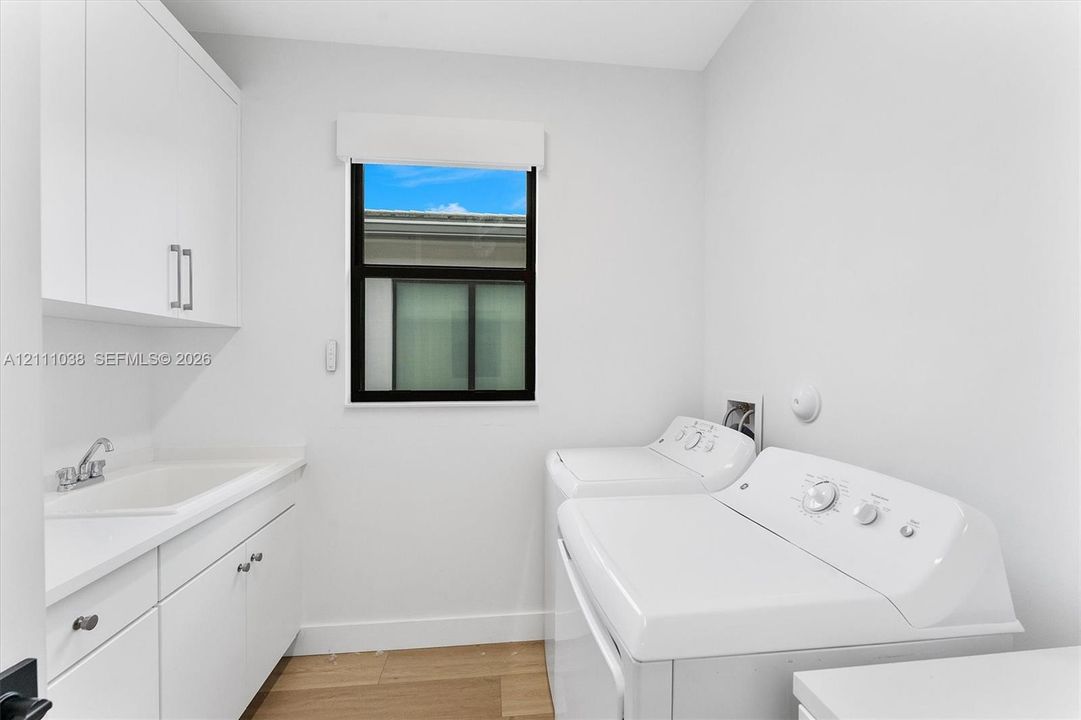 Laundry room featuring white cabinetry, integrated sink with chrome faucet, wood-finish flooring, and single-pane window with black framing