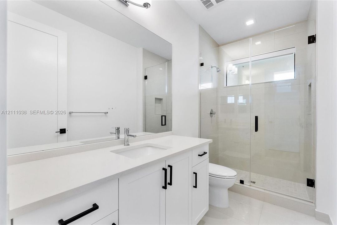 White cabinetry vanity with solid surface countertop, glass-enclosed shower with tiled walls and built-in niche, and matte black hardware fixtures