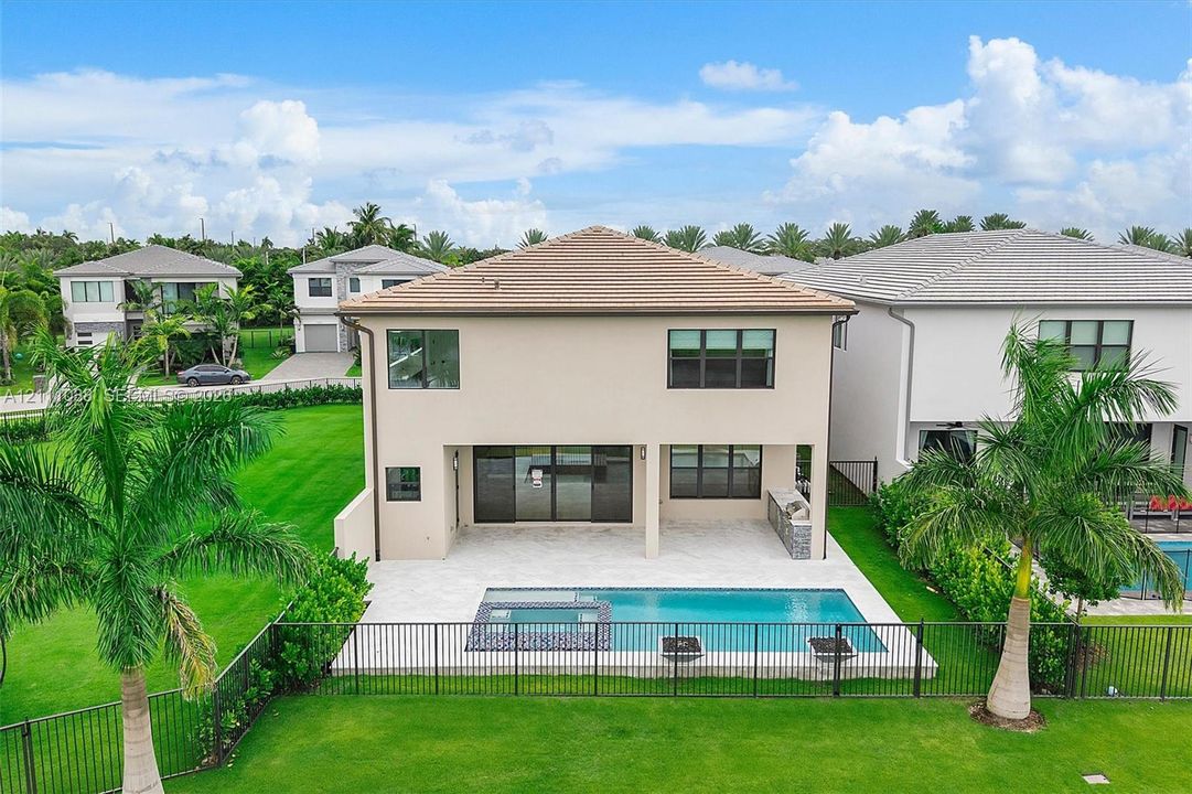 Rear exterior featuring a covered patio, built-in outdoor kitchen, in-ground swimming pool with spa, and fenced-in lawn area