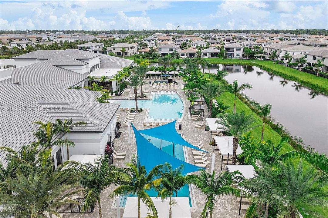 Resort-style swimming pool, expansive paver patio, integrated shade structures, tropical landscaping, and waterfront scenery