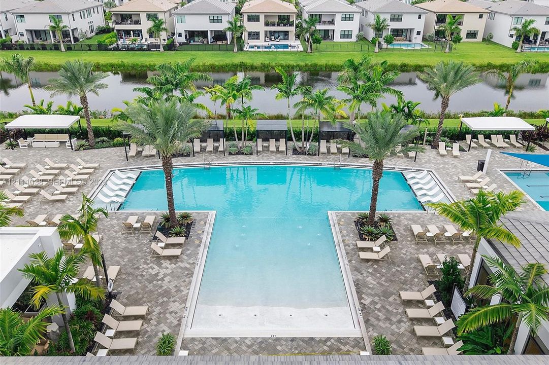 Community pool featuring a shallow sun shelf, paver surround, mature palm trees, and covered cabanas