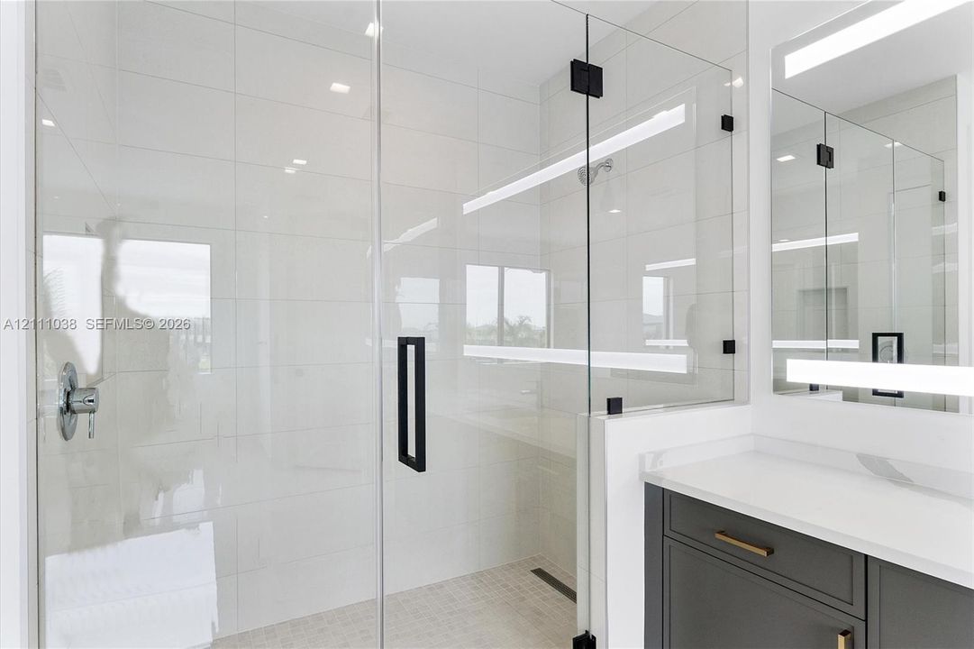 Walk-in shower with floor-to-ceiling tile, frameless glass enclosure, and matte black hardware, featuring a modern vanity with a white countertop and integrated linear LED mirror lighting