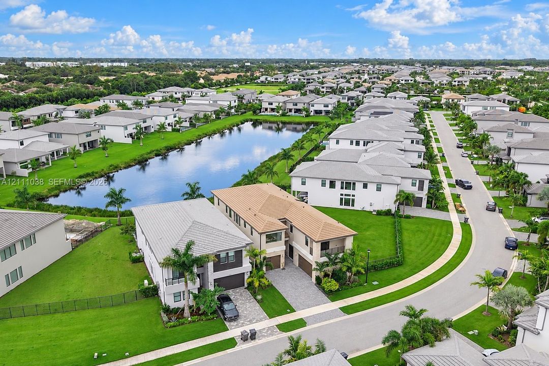 Aerial perspective of a two-story residence featuring a tiled roof, paver driveway, and a backyard oriented toward a central pond
