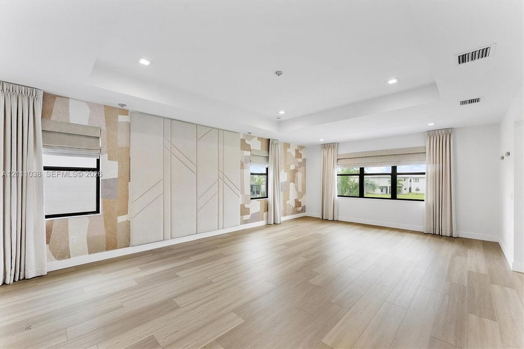 Tray ceiling featuring recessed lighting, light wood-finish flooring, and wall panels with textured geometric detailing