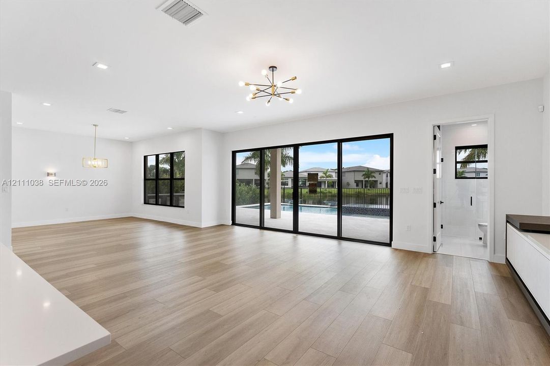 Open-concept interior featuring light wood-finish flooring, multi-panel sliding glass doors with black frames, recessed lighting, and modern multi-arm chandeliers