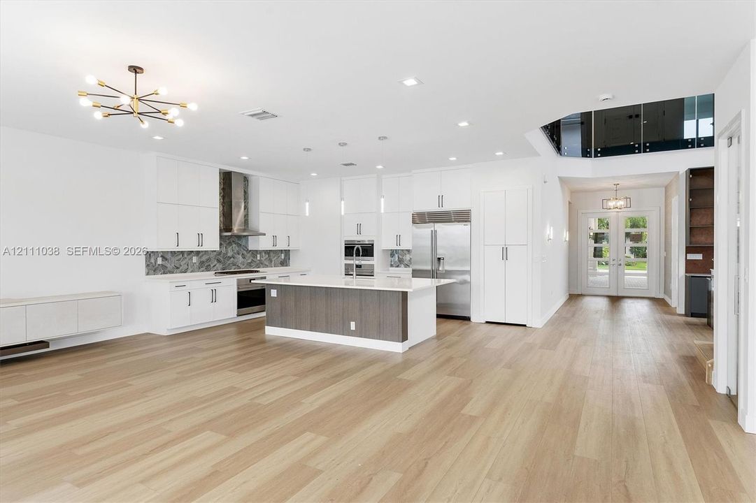 Kitchen featuring white flat-panel cabinetry, wood-finish flooring, a center island with contrasting cabinetry, stainless steel appliances, and a glass-paneled mezzanine level