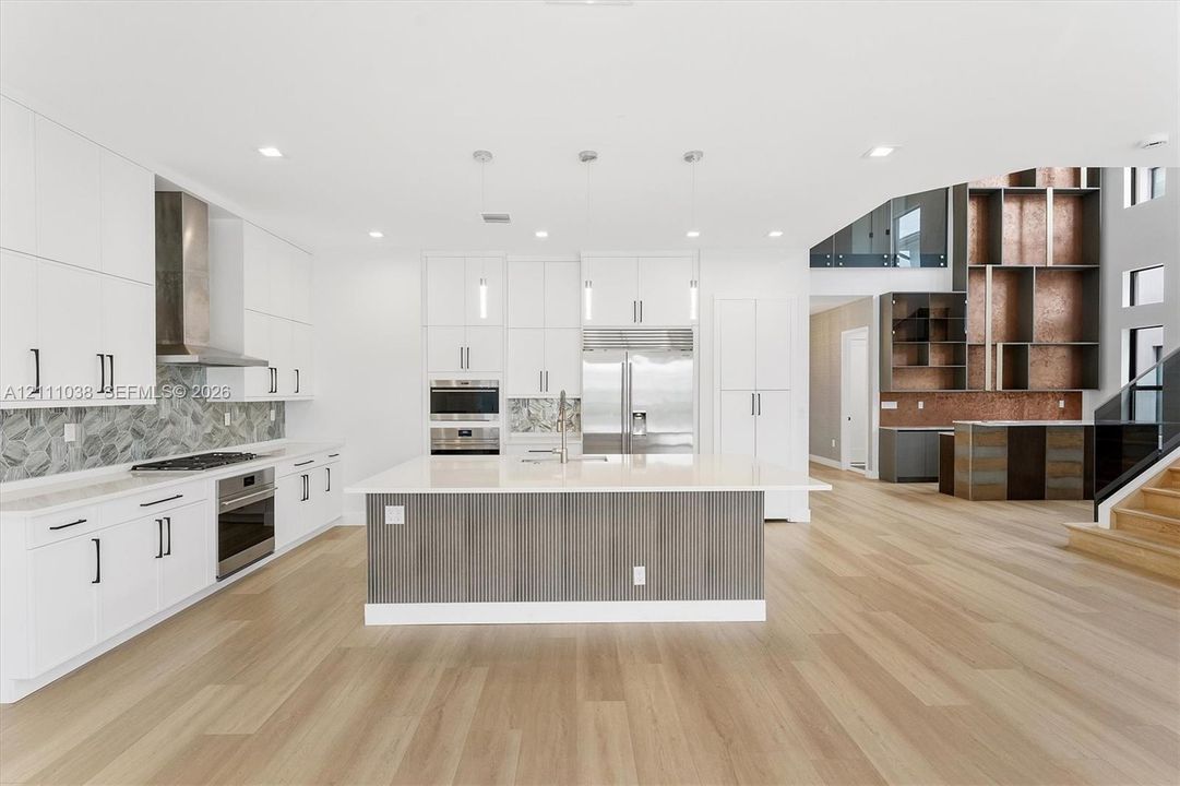 Kitchen featuring white cabinetry, wood-finish flooring, a central island with a solid-surface countertop, stainless steel appliances, and a decorative tile backsplash