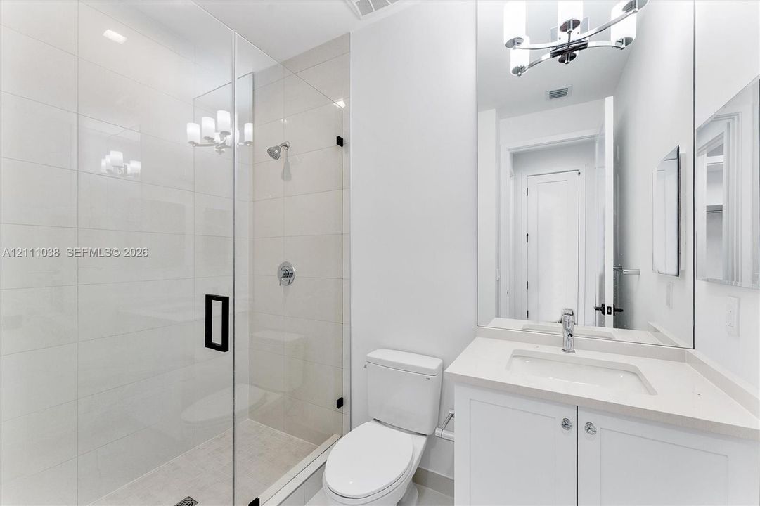 Walk-in shower with floor-to-ceiling tile, frameless glass enclosure, and matte black hardware, paired with a white vanity featuring a stone-composite countertop and an expansive wall-mounted mirror