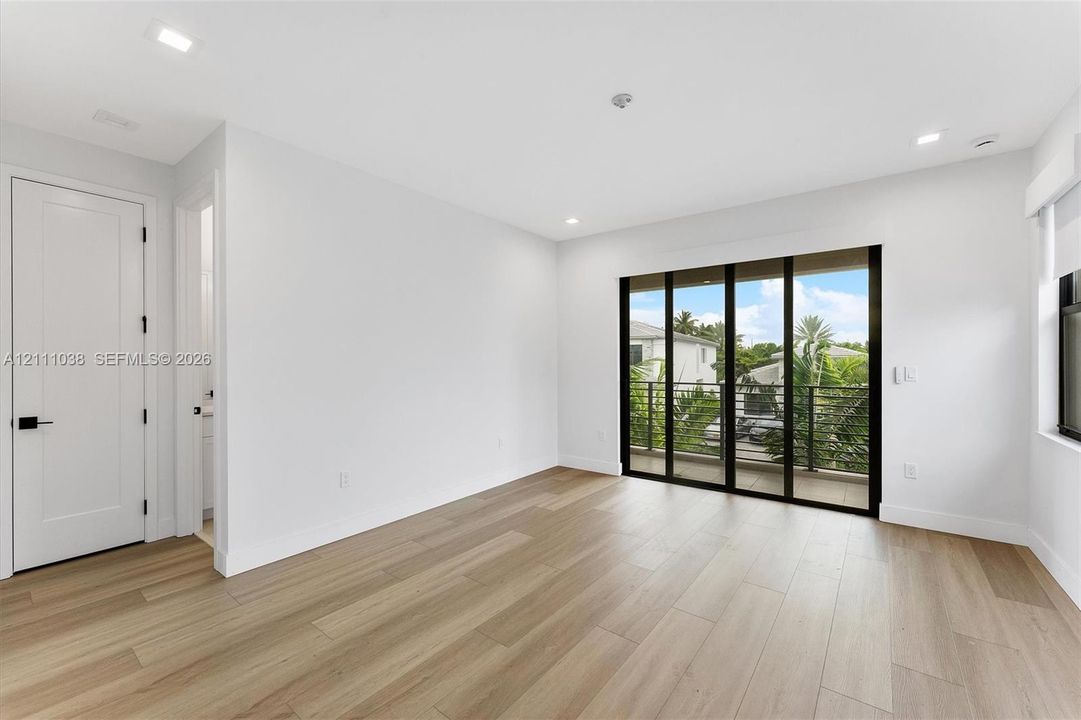 Wood-finish flooring, recessed lighting, multi-panel sliding glass doors with black frames, and a private balcony