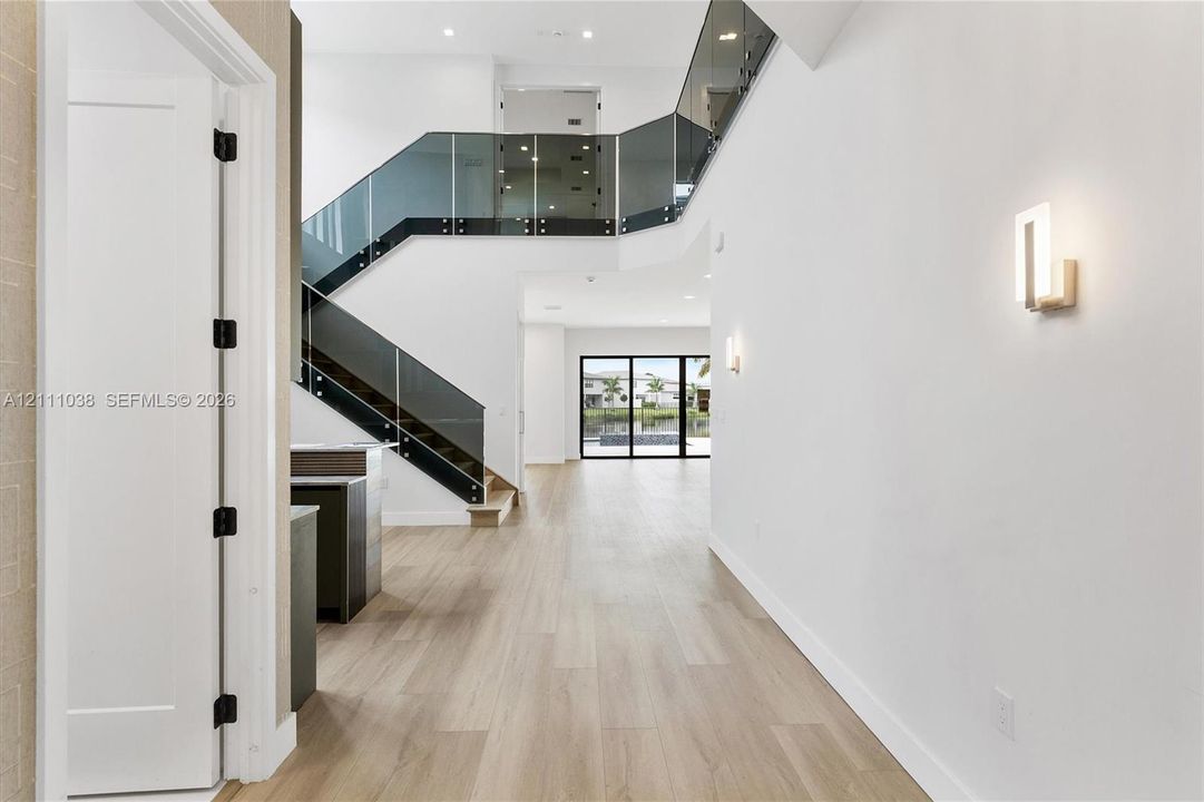 Two-story foyer featuring wood-finish flooring, a glass-paneled staircase with metal hardware, recessed lighting, and modern wall-mounted light fixtures
