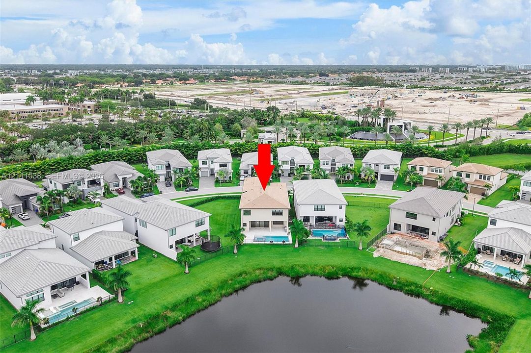 Two-story residence featuring a tile roof, an in-ground swimming pool, and water frontage on a decorative pond, situated on a manicured lot with mature palm trees