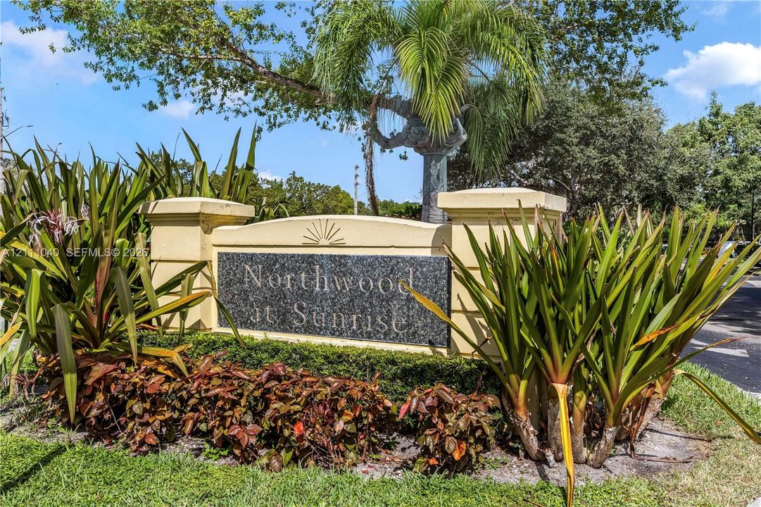 Monument-style community entrance sign featuring a stone plaque, stucco pillars, and landscaped garden beds