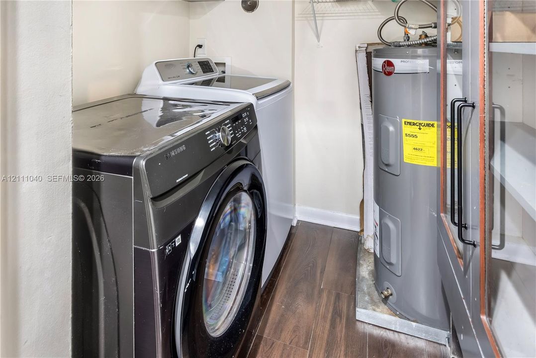 Laundry area featuring wood-finish flooring, built-in shelving with matte black hardware, and an electric water heater