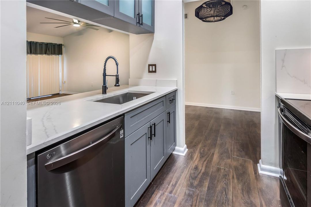 Kitchen featuring grey shaker-style cabinetry, white countertops with grey veining, a stainless steel undermount sink, a pull-down faucet, and wood-finish flooring