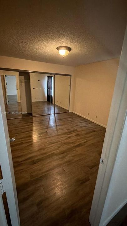 Room featuring wood-finish flooring, ceiling-mounted light fixture, and floor-to-ceiling mirrored closet doors