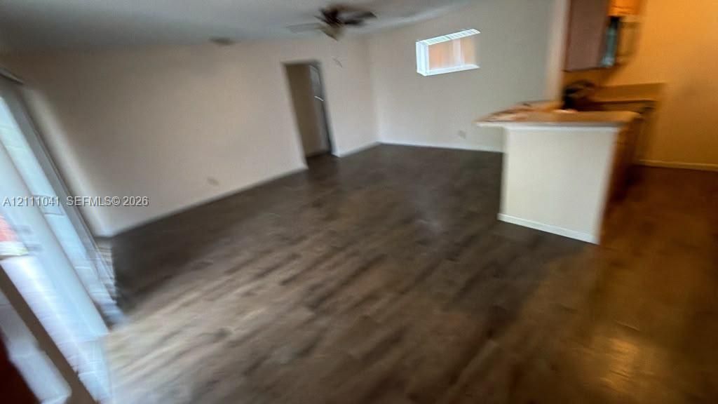Open-concept interior featuring wood-finish flooring, a kitchen breakfast bar, sliding glass door, and a ceiling fan