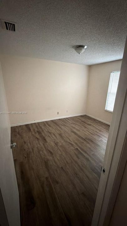 Interior room featuring wood-finish flooring, a single window, and a flush-mount ceiling light fixture