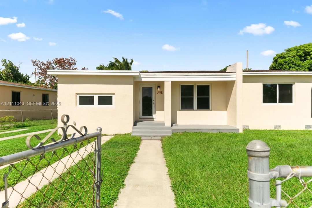 Single-story residence featuring a smooth stucco exterior, covered entryway with concrete steps, and a metal chain-link perimeter fence
