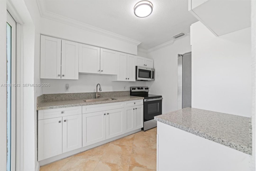 Kitchen featuring white shaker-style cabinetry, stone-finish countertops, stainless steel appliances, a high-arc faucet, and tiled flooring