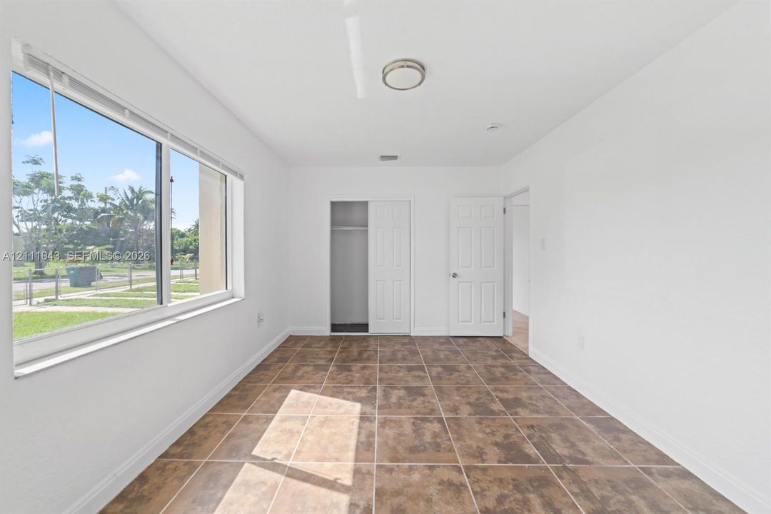 Interior space featuring large-format ceramic tile flooring, neutral walls, sliding-door closet, and large-pane window with blinds