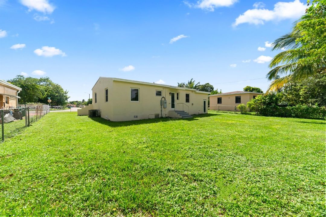 Expansive grass yard featuring perimeter chain-link fencing, stucco exterior finish, and mature palms