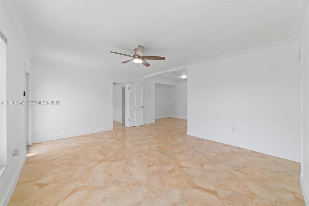 Interior space featuring neutral-toned tile flooring, crown molding, and a central ceiling fan with an integrated light fixture