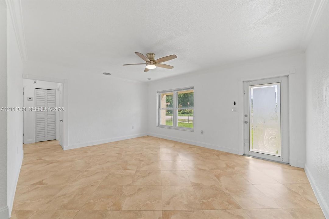 Neutral-toned tile flooring, ceiling fan with integrated lighting, dual-pane window, and exterior door with frosted glass inlay and closet with louvered doors