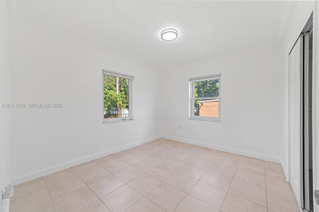 Neutral interior featuring tile flooring, smooth ceiling with a flush-mount light fixture, two windows with horizontal blinds, and a sliding closet door