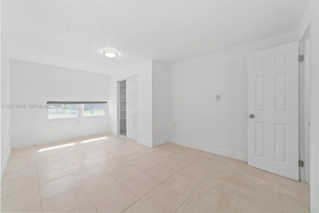 Interior space featuring large-format neutral tile flooring, crisp white wall finishes, a built-in closet with double-panel doors, and a flush-mount circular ceiling fixture