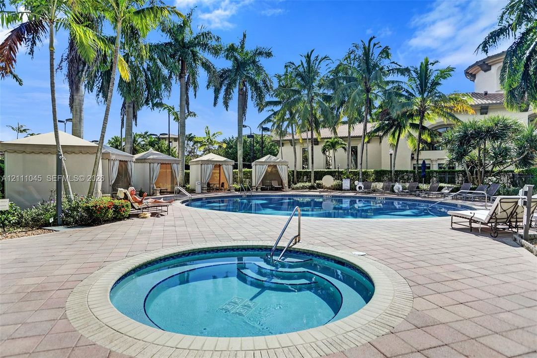 Swimming pool and circular spa surrounded by paver patio, multiple poolside cabanas, and mature palm trees