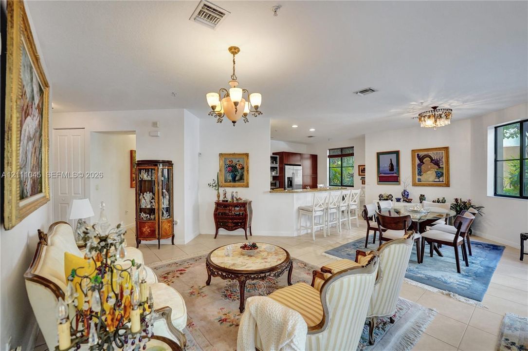 Open-concept interior featuring light-toned tile flooring, recessed lighting, and dual multi-arm chandeliers