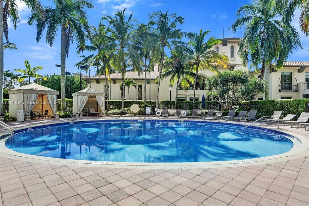 Circular swimming pool featuring a paved stone deck, dual shaded cabanas, and manicured palm tree landscaping