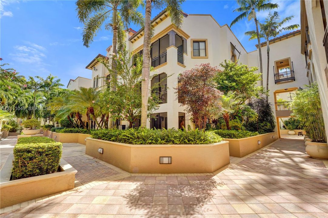 Mediterranean-style exterior featuring stucco facade, multi-level screened balconies, paver walkways, integrated landscape lighting, and raised masonry planters